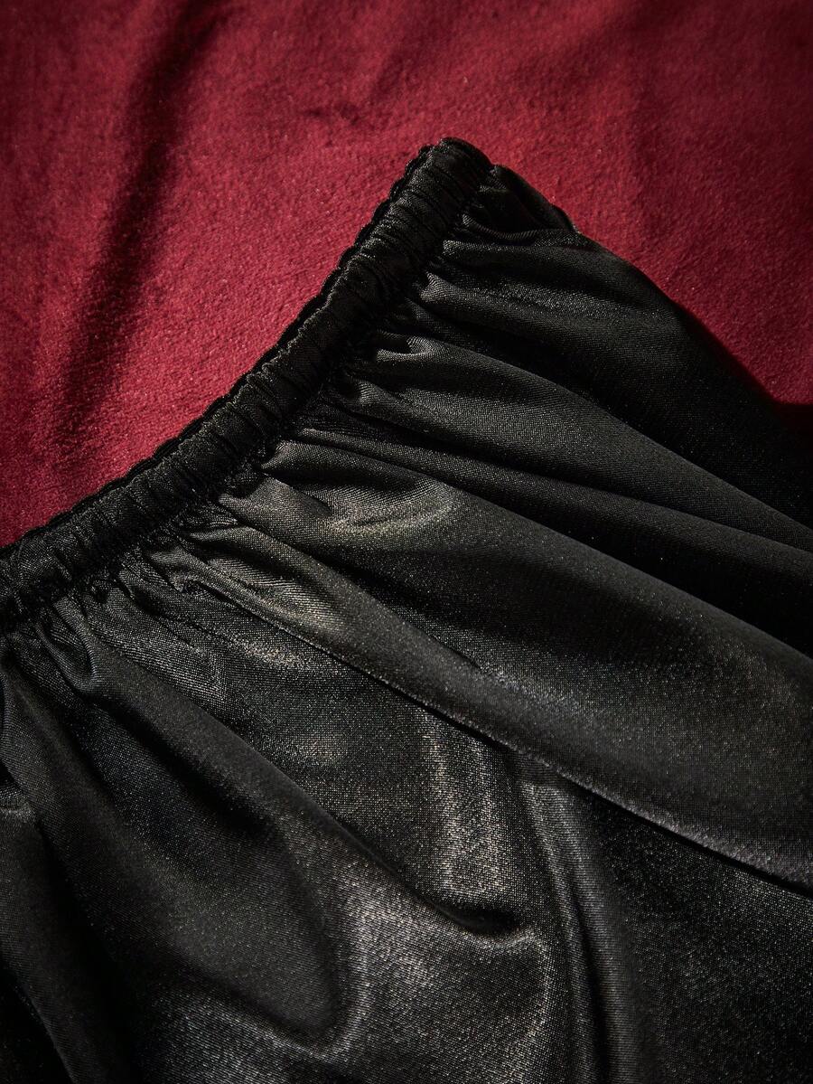 A 2-piece women's black gothic lingerie set featuring a halter bralette top with bow tie and heart detail paired with matching ruffled mid-rise boyshorts.