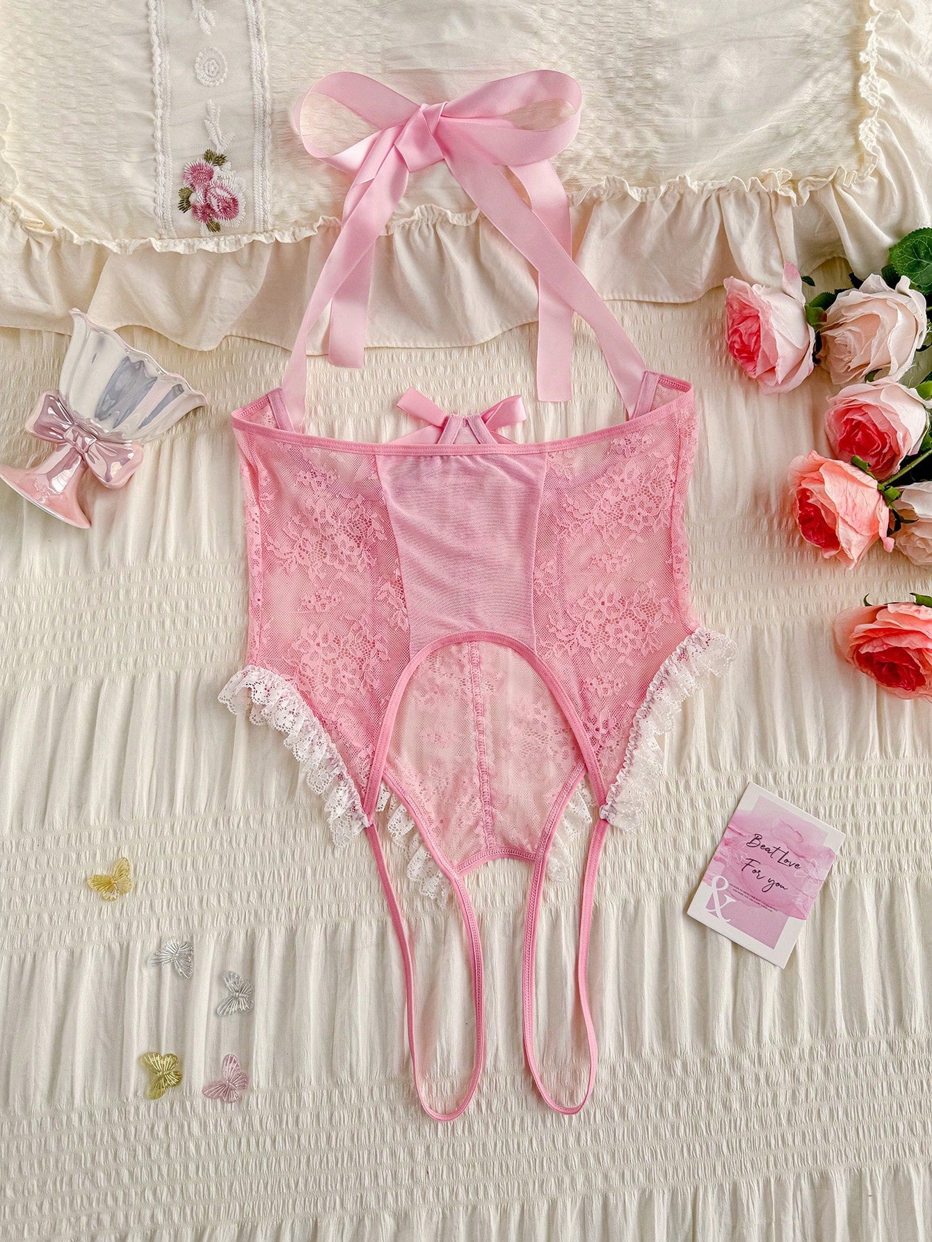 Pink lace lingerie jumpsuit for women with halter neckline, backless design, adjustable straps, ruffle hem, semi-sheer fabric, and thong bottom.