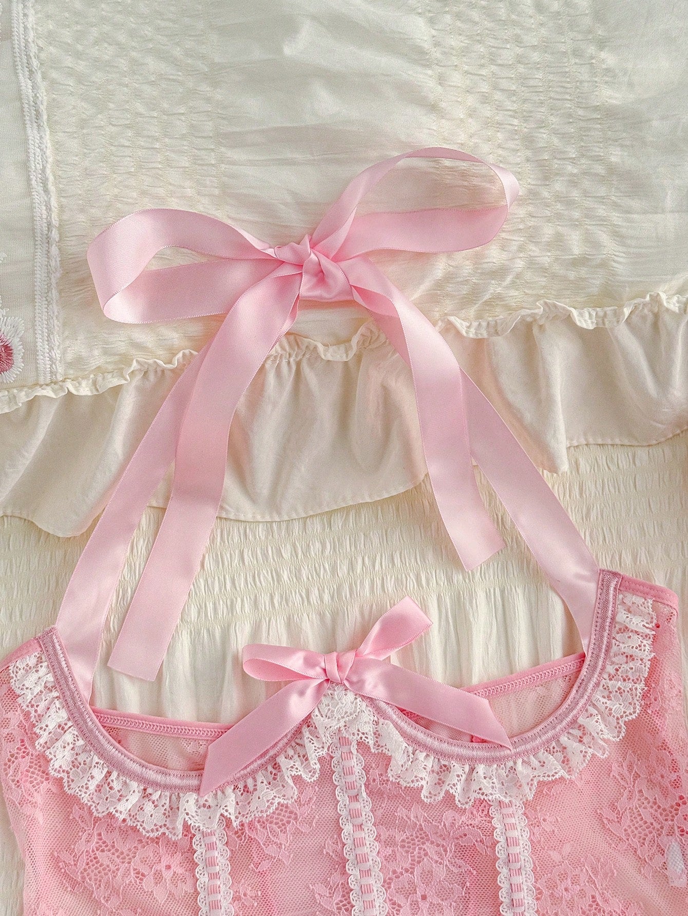 Pink lace lingerie jumpsuit for women with halter neckline, backless design, adjustable straps, ruffle hem, semi-sheer fabric, and thong bottom.