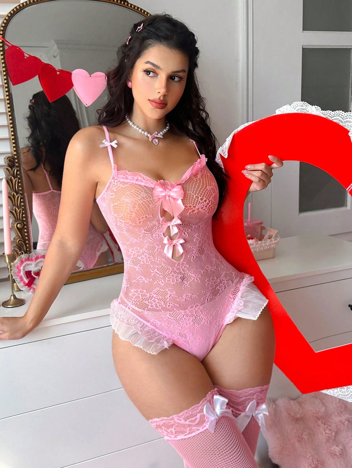 Pink women's fishnet bodystocking in sheer mesh with contrast lace, bow detail, adjustable spaghetti straps, and sleeveless wireless teddy bodysuit design.