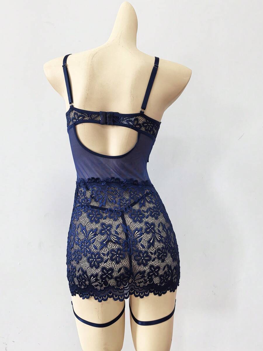 Woman wearing a sheer black lace patchwork mesh nightgown featuring underwire cups, adjustable spaghetti straps, matching thong, and leg rings.